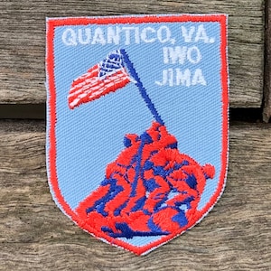 May include: A blue and red embroidered patch with the text "Quantico, VA. Iwo Jima" and a depiction of the raising of the American flag on Iwo Jima.