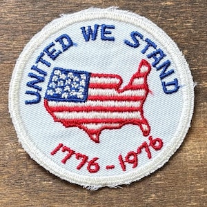 Peut inclure: Écusson brodé circulaire avec l'inscription "UNITED WE STAND" en bleu. Il représente un contour rayé rouge et blanc des États-Unis avec un drapeau bleu et blanc. Les chiffres "1776-1976" sont en rouge. L'écusson a une bordure blanche.