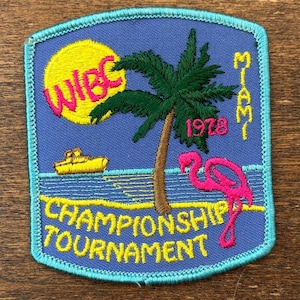 May include: A blue patch featuring a yellow sun, palm tree, and a pink flamingo. The patch reads "WBC", "Miami 1978", and "Championship Tournament" in yellow text. A yellow boat sails on the water.