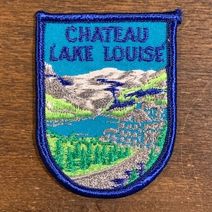May include: A blue and white embroidered patch with the text "Chateau Lake Louise" and a scenic image of a lake, mountains, and trees.