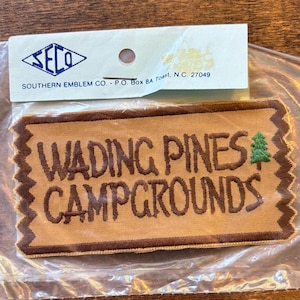 May include: A rectangular patch with the text "WADING PINES CAMPGROUNDS" in brown lettering. A green tree graphic is on the right. The patch is tan with a brown border and a jagged edge.