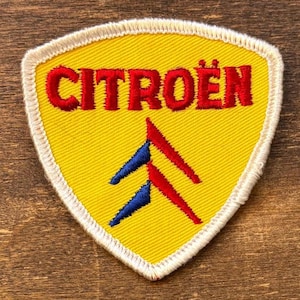May include: Yellow embroidered patch with the word "CITROËN" in red, and a red and blue logo. The patch has a white border and a shield shape.