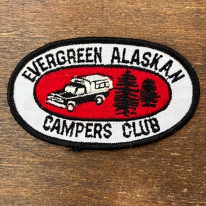 Puede incluir: Parche ovalado con el texto "EVERGREEN ALASKAN CAMPERS CLUB". El parche presenta un óvalo rojo con una furgoneta camper negra y blanca y dos pinos. El borde es negro y blanco.