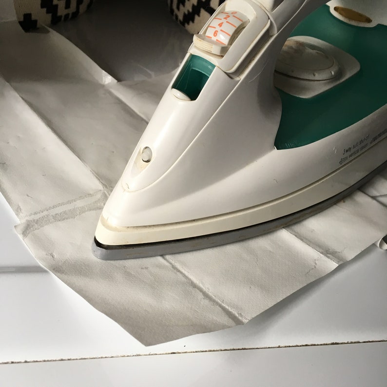 May include: A white and teal iron with a temperature dial set to 3. The iron is resting on a white piece of paper.