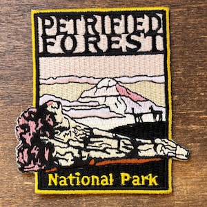 Puede incluir: Parche bordado con las palabras "PETRIFIED FOREST" sobre un paisaje con una montaña y árboles. Las palabras "National Park" están en la parte inferior. El parche tiene un borde negro con costuras amarillas.