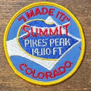 Op de afbeelding: Een ronde patch met een blauwe achtergrond en een gele rand. De patch bevat de tekst "I MADE IT" en "SUMMIT PIKES PEAK 4300 m COLORADO" in rood en wit. Een bergafbeelding staat in het midden.