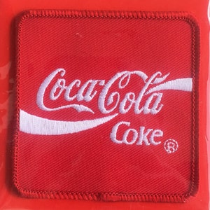 May include: Red fabric patch with white embroidered Coca-Cola logo and the word "Coke" with a registered trademark symbol.