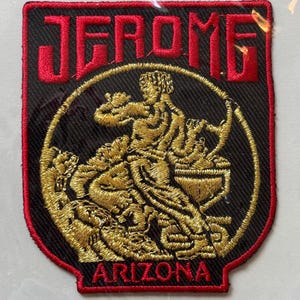 Puede incluir: Parche bordado con la palabra "JEROME" en letras rojas en la parte superior y "ARIZONA" en la parte inferior. El parche presenta una figura dorada dentro de un círculo negro.
