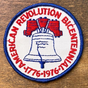Peut inclure: Un écusson brodé circulaire avec un fond blanc et une bordure bleue. Le centre présente un motif de Liberty Bell en rouge et bleu. Le texte AMERICAN REVOLUTION BICENTENNIAL 1776-1976 est brodé en rouge sur le pourtour de l'écusson.