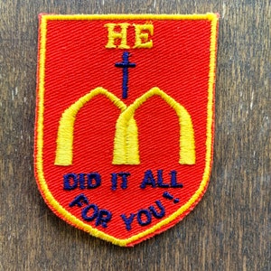 May include: Embroidered red patch with yellow and blue accents. The patch features the text "HE" above a blue cross and two yellow arches. Below the arches, the text reads "DID IT ALL FOR YOU!" in blue.