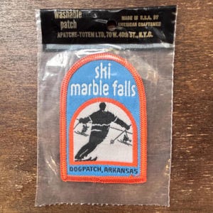 Op de afbeelding: Een blauwe en oranje geborduurde patch met een skiër in silhouet op een witte achtergrond. De tekst luidt "ski marble falls DOGPATCH, ARKANSAS".