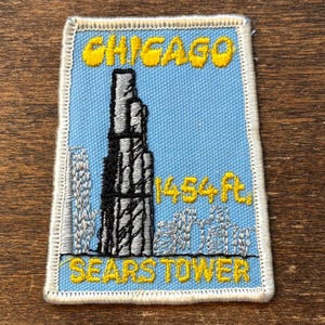 Puede incluir: Parche bordado con la Torre Sears en Chicago. El parche tiene un fondo azul claro con texto amarillo que dice "CHICAGO" y "SEARSTOWER". La torre es negra y gris, con la altura de 443,2 m también en amarillo.