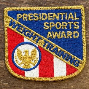 May include: Embroidered patch with the text "PRESIDENTIAL SPORTS AWARD WEIGHT TRAINING". The patch features a blue and red design with a gold eagle emblem and gold border. A vintage sports award.