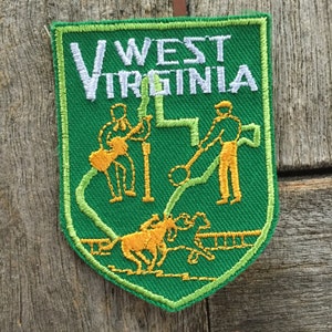 May include: Green embroidered patch with the text "WEST VIRGINIA" in white. The patch features a stylized outline of the state of West Virginia with yellow figures of people and animals.