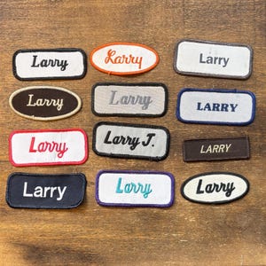 May include: A collection of embroidered patches with the name "Larry" in various fonts and colors. The patches are rectangular and oval, with different border colors like black, red, and blue. Some patches have a cursive font.