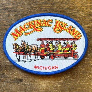 May include: Oval patch with a blue border featuring the words "Mackinac Island" in yellow and red. The patch depicts a horse-drawn carriage with passengers. The word "Michigan" is printed at the bottom.