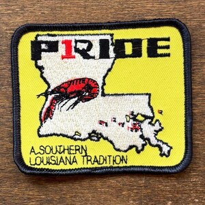 May include: Embroidered patch with a yellow background and a black border. The patch features the word "PRIDE" with a red "1" and a map of Louisiana. A red and black crawfish is on the map, with the text "A SOUTHERN LOUISIANA TRADITION".
