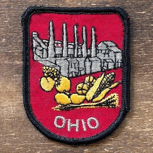 May include: Embroidered patch featuring a red background with a black border. The patch depicts a factory scene with smokestacks, along with yellow corn and other produce. The word "OHIO" is embroidered in white.