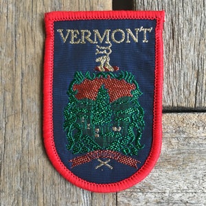 May include: An embroidered patch in blue and red with the word "VERMONT" in gold lettering and a green and red embroidered state seal.