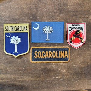 Op de afbeelding: Een verzameling geborduurde patches met de symbolen van de staat South Carolina. De patches bevatten de staatsvlag, een schild met een palmetto-boom en een halve maan, en de tekst "SOUTH CAROLINA" en "SOCAROLINA".