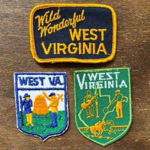 Könnte beinhalten: Drei gestickte Aufnäher mit Motiven aus West Virginia. Ein Aufnäher trägt die gelbe Aufschrift "Wild Wonderful WEST VIRGINIA" auf marineblauem Grund. Die anderen beiden Aufnäher zeigen Illustrationen und die Texte "WEST VA" und "WEST VIRGINIA".
