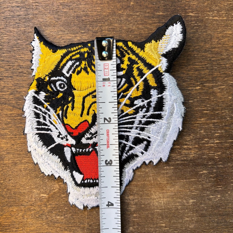 May include: An embroidered tiger head patch featuring yellow, black, white, and red thread. A white measuring tape is placed vertically over the center of the patch, indicating a height of approximately 4 inches from top to bottom.