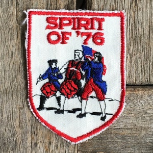 Peut inclure: Un écusson brodé blanc avec des coutures rouges. L'écusson présente un motif rouge, blanc et bleu avec trois personnages en marche. Le texte "SPIRIT OF '76" est brodé en rouge.