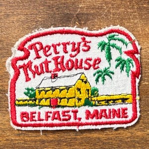 May include: Embroidered patch featuring the text "Perry's Nut House" in red script, with a yellow building and green palm trees. The patch also includes the text "Belfast, Maine" in red.