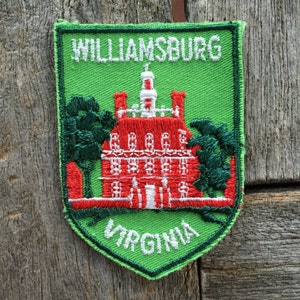 May include: Green and red embroidered patch with the text "Williamsburg, Virginia". The patch features a red building with white trim and green trees.