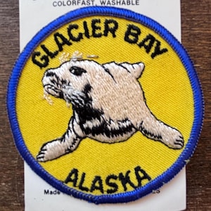 May include: A yellow and blue embroidered patch with the text "Glacier Bay Alaska" and a white and black sea lion illustration.
