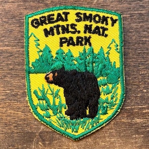 May include: Embroidered patch featuring a black bear in front of green trees and foliage, with the text "GREAT SMOKY MTS. NAT. PARK" in yellow. The patch has a yellow background and a green border.
