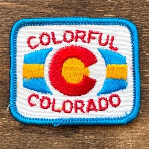 Könnte beinhalten: Gestickter Aufnäher mit weißem Hintergrund und blauem Rand. Der Aufnäher zeigt das Wort "COLORFUL" oben und "COLORADO" unten in roten Buchstaben. Ein rotes und gelbes "C" befindet sich in der Mitte, mit blauen und gelben Akzenten auf beiden Seiten.