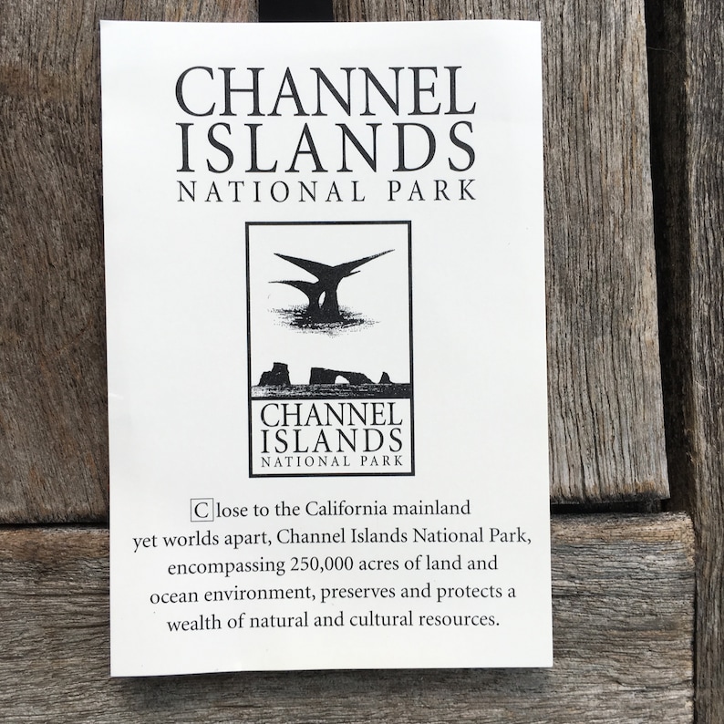 Op de afbeelding: Zwart-wit logo voor Channel Islands National Park. Het logo toont een gestileerde afbeelding van een eiland met een vogel die erboven vliegt. De tekst "Channel Islands National Park" staat onder de afbeelding.