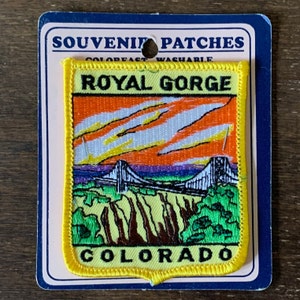 Op de afbeelding: Gele geborduurde patch met een zonsondergangsscene van een brug over een canyon. De tekst "Royal Gorge Colorado" staat op de patch.