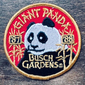 May include: An embroidered patch featuring a panda bear with the text "Giant Panda" and "Busch Gardens" in gold lettering. The patch also includes the years "'87" and "'88" in gold lettering.
