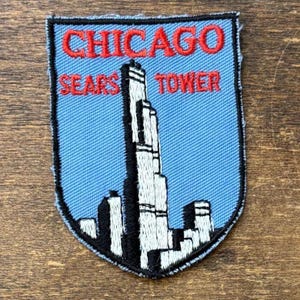 Op de afbeelding: Een schildvormige geborduurde patch met een lichtblauwe achtergrond en een zwarte rand. Het bevat een witte en zwarte afbeelding van de Sears Tower in Chicago. De rode geborduurde tekst luidt CHICAGO bovenaan en SEARS TOWER in het midden.