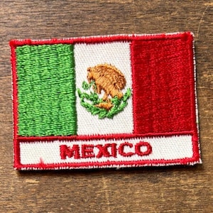Könnte beinhalten: Gestickter Aufnäher mit der mexikanischen Flagge. Das Design umfasst grüne, weiße und rote vertikale Streifen mit dem mexikanischen Wappen in der Mitte. Das Wort "MEXICO" ist unten aufgestickt.