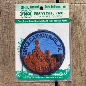 Puede incluir: Un parche bordado azul y marrón con el texto "Bryce Canyon Nat'l Pk" y "Utah" sobre un fondo blanco. El parche está empaquetado en una bolsa de plástico con una tarjeta blanca que dice "Official, National Park Emblems 98c TWA SERVICES, INC. UTAH PARKS DIVISION Zion, Bryce, Grand Canyon (North Rim) National Parks Emblem by A-B Emblem Corp., Weaverville, N. C. 28787".