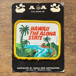 May include: Vintage Hawaii patch featuring a tropical landscape with palm trees, a river, and the text "HAWAII THE ALOHA STATE" in red. The patch has a yellow border and is on a black backing with the AA Sales Inc. logo.