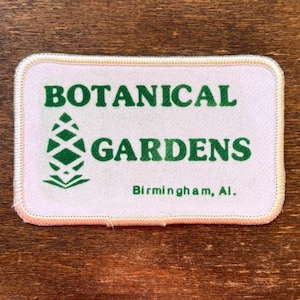 May include: A rectangular patch with rounded corners, featuring the words "BOTANICAL GARDENS" in green, along with a green graphic of a stylized plant. The text "Birmingham, Al." is below. The patch has a white background with a pink border.