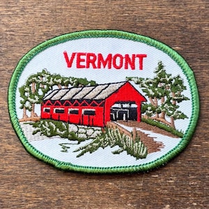 May include: Oval patch with a red covered bridge and the word "VERMONT" in red. The bridge is set amongst trees and greenery, with a green border.