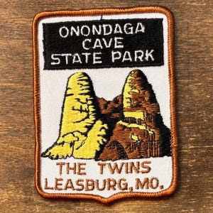 May include: Embroidered patch featuring the text "ONONDAGA CAVE STATE PARK" above an illustration of two rock formations. Below the illustration is the text "THE TWINS LEASBURG, MO." The patch has a white background with a brown border.