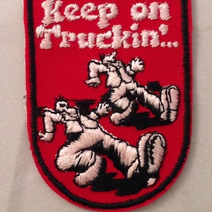 May include: A red embroidered patch with a black border featuring the white text Keep on Truckin... and two stylized figures in white thread with black accents, depicted in a dynamic walking motion across the center of the patch.