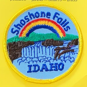 Op de afbeelding: Een blauw en geel geborduurd patch met een regenboog boven een waterval en de tekst "Shoshone Falls IDAHO".