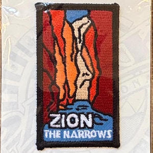 May include: Rectangular patch with a design featuring a stylized mountain or rock formation in orange, white, and red, set against a blue and red background. The text "ZION THE NARROWS" is displayed in white letters.