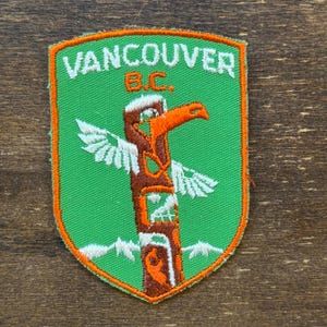 May include: A green and orange embroidered patch with the text "Vancouver B.C." and a stylized totem pole with a bird on top.