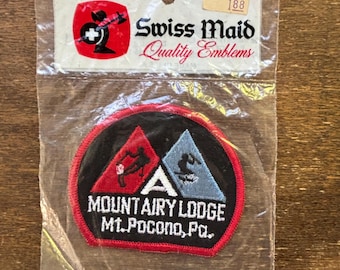 Könnte beinhalten: Ein gestickter Aufnäher in Rot, Weiß und Blau mit dem Text "Mountairy Lodge Mt. Pocono, Pa." und zwei Skifahrern in der Mitte. Der Aufnäher ist in einer durchsichtigen Plastiktüte mit einem weißen Etikett verpackt, auf dem "Swiss Maid Quality Emblems 188" steht.