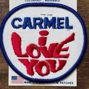 May include: A white, round, embroidered patch with a blue border. The patch says "CARMEL I LOVE YOU" in red and blue thread.
