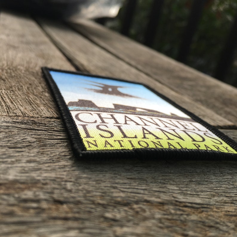 Op de afbeelding: Een zwart en groene patch met witte tekst die "Channel Islands National Park" luidt. De patch heeft een blauwe achtergrond met een witte afbeelding van een rotsachtig eiland.