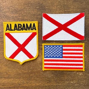 May include: Three embroidered patches: one with "ALABAMA" and a red cross on a white shield, another with a red cross on white, and a third with the American flag design. All have yellow borders.